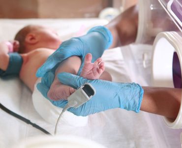 Three-day-old newborn baby in intensive care unit in a medical incubator. Macro photo of doctor's hands and legs of a child. Newborn rescue concept. The work of resuscitation doctors. Photo indoors.